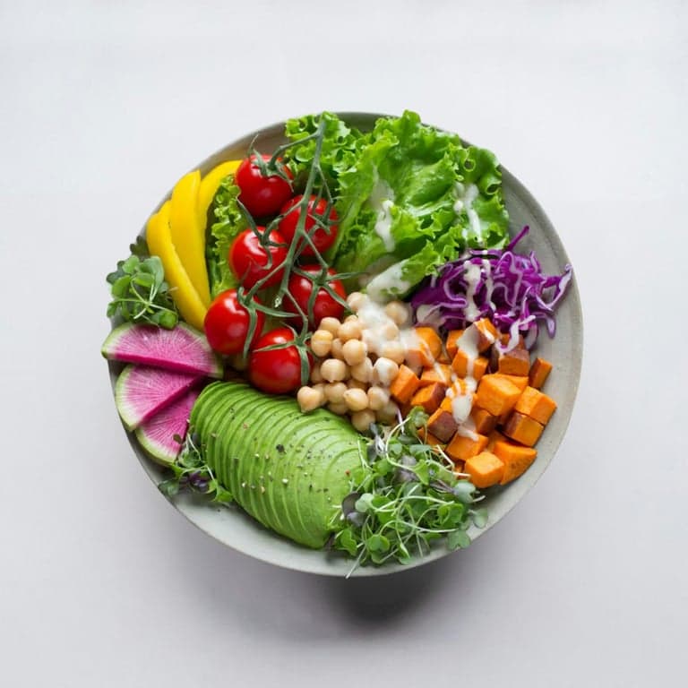 A bowl of leafy greens, sweet potato, avocado and seeds